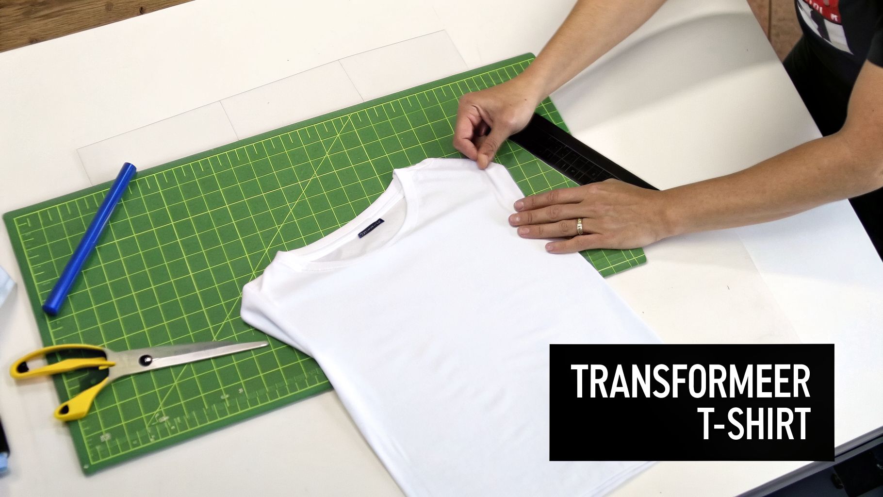 Persoon legt een wit T-shirt netjes op een groene snijmat, omringd door schaar en liniaal.