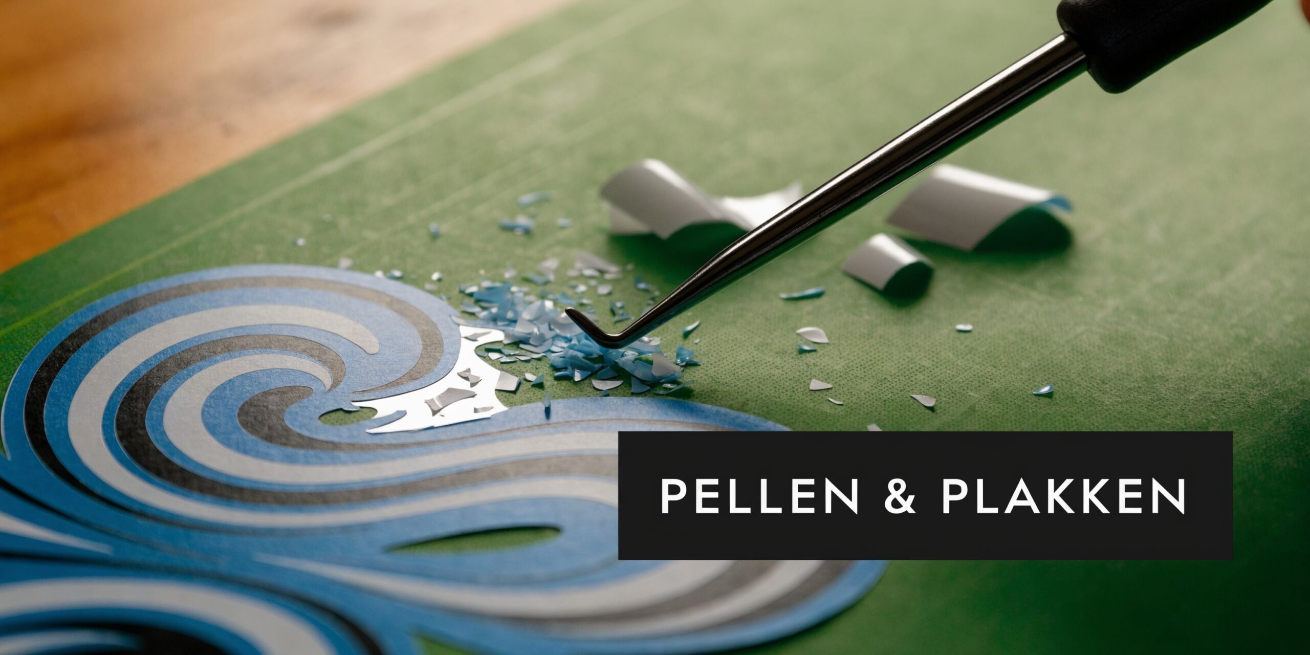 Een detailopname van een ambachtsman die overtollig vinyl verwijdert van een zelfklevende sticker met een metalen pelhaak.