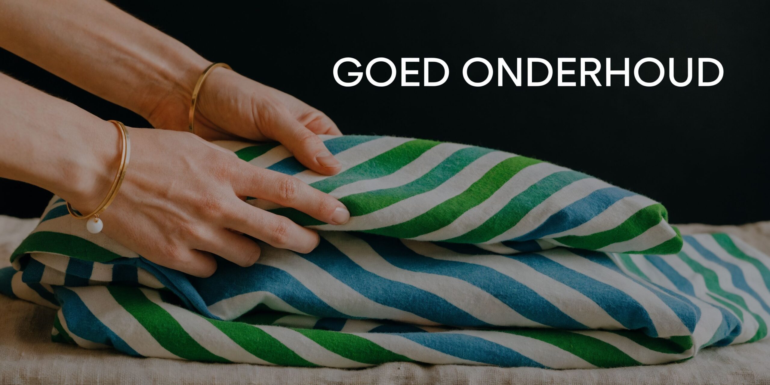 Een persoon vouwt een katoenen stof met groene en blauwe strepen netjes op een beige ondergrond.