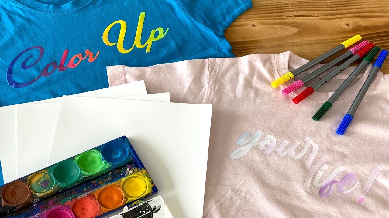 Welke printbare flexfolie past het beste bij jouw project? 4 Materialen voor een creatief project, met blauwe en roze T-shirts, waterverf, stiften en papier om te kleuren op printbare flex