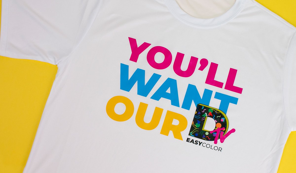 Welke printbare flexfolie past het beste bij jouw project? 2 Een witte t-shirt met de kleurrijke tekst 'YOU'LL WANT OUR D' en 'EASYCOLOR tv' op een gele achtergrond.